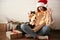 Stylish happy girl in santa hat  and cute cat waving hand and paw in festive christmas lights on background of modern presents.