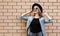 Stylish happy smiling young woman looking up wearing a black round hat, jeans jacket, female model on brick wall