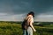 Stylish hiker girl in casual clothes and backpack walks on the mountain on a background of rainbow and blue rain clouds. Domestic