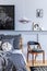 Stylish hipster bedroom interior with design chair, mock up poster frames, book, clock, decoration, carpet, beautiful bed sheets.