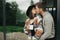 Stylish hipster couple with morning coffee kissing on background of modern cabin with big windows in mountains. Happy young family