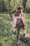 stylish hipster girl in hat with backpack walking in woods in evening sunshine. woman traveler back view in sunlight among trees.