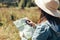 Stylish hipster girl holding map and compass, traveling in sunny mountains. Woman in hat exploring map and hiking on top of