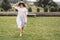 Stylish hipster girl in linen dress and hat having fun at lavender field and relaxing in mountains. Bohemian woman smiling and