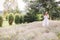 Stylish hipster girl in linen dress and hat relaxing in lavender field near tree, focus on lavender. Bohemian woman enjoying