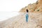 Stylish hipster girl running barefoot on beach at sea , back view. Happy fashionable boho woman relaxing at sandy cliff on