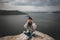 Stylish hipster girl with windy hair sitting on top of rock mountain with beautiful view on river. Young tourist woman relaxing on