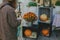 Stylish hipster woman taking photo of pumpkins and autumn flowers on wooden boxes. Girl photographing on phone rustic halloween