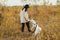 Stylish hipster woman training cute white dog on background of autumn trees. Traveling with pet
