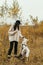 Stylish hipster woman training cute white dog on background of autumn trees. Traveling with pet