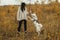 Stylish hipster woman training cute white dog on background of autumn trees. Traveling with pet