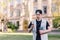 A stylish, interested student in a cap wears a mobile phone and listens to music at the background of the university