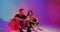 Stylish joyful young teen couple talking sitting on floor in colourful neon studio light. Romantic dating and flirting