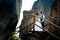 Stylish just married couple is tenderly holding hands while standing on the wooden stairs between two rocks. Sunny