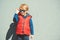 Stylish kid in trendy sunglasses. Kids fashion. Cute little blondy boy in red jacket standing over grey wall outdoors in sunny day