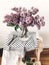 Stylish lilac purple bouquet in glass vase on rustic wooden ladder with fabric in room. Fresh spring lilac flowers bouquet on