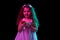Stylish little girl, beginner fashion model using phone isolated over dark background in neon light. Children emotions