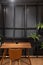 Stylish loft working corner with wood table, leather chair and artificial plant with black metal rod on the background / interior
