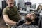 Stylish man with a beard sits at a barbershop. Barber trims mens beard with scissors.