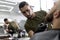 Stylish man with a beard sits in front of the mirror at a barbershop. Barber trims mens beard with scissors