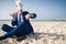 Stylish man in funny mask and elegant suit sits on beach