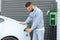 Stylish man inserts plug into the electric car charging socket