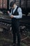 stylish man in retro look smiling posing on background of railway. england in 1920s theme. fashionable brutal confident gangster.