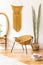Stylish and minimalist interior of living room with design gold armchair, lamp, poster frames. dressing table with mirror, plants.