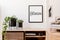 Stylish minimalistic living room interior with mock up poster frame, commode, plants in black pots and accessories. White walls.