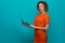 Stylish model in orange dress posing with laptop.