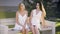 Stylish models in white dresses posing on bench in park and talking lively.