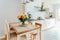 Stylish and modern boho, scandi interior of open space white kitchen with yellow and orange roses flower in vase on the