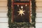 Stylish modern christmas star hanging in window with spruce branches on old building or shop. Merry Christmas. Illuminated sweden