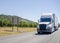 Stylish modern white big rig semi truck with dry van semi trailer transporting cargo running on the road along the orchards in