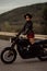 Stylish motorcyclist woman in mini skirt, leather jacket stands on vintage-styled motorcycle. Attractive alluring driver