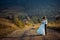 Stylish newlywed couple is hugging on the road at the background of the beautiful mountains during the sunset.