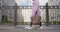 Stylish person in pink coat and carrying large leather bag walks along the street along an iron fence, behind which