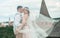 Stylish portrait happy newlyweds bride and groom wrapped in a veil embracing each other on the background of castle