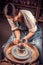 Stylish pottery woman siting on bench with pottery wheel and making clay pot. National craft.