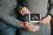 Stylish pregnant couple holding ultrasound scan of baby on baby bump. Healthy young parents holding in hands on belly photo of