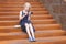 Stylish preteen girl using a phone sitting on a rusty staircase. Child and gadget concept.