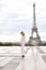 Stylish pretty woman standing near Eiffel Tower in white overalls.
