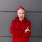 Stylish pretty young woman in modern fashionable clothes with a red bandanna is standing near a gray modern building