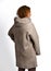 Stylish red-haired curly woman poses back to us in modern grey oversize sheepskin coat with hood on white