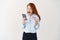 Stylish redhead girl staring surprised at smartphone screen while shopping online, holding plastic card, reaction on