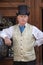 A stylish retro vintage fashionable gentleman in a waistcoat and a bowler hat invites tourists to enter the restaurant on the stre