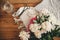 Stylish Scissors, fabric, pink and white peonies and glass vase on wooden floor, top view. Florist and floral shop