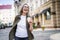 Stylish senior woman with grey hair holding coffee cup while enjoying vibrant atmosphere of European city. Colorful