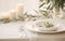 Stylish setting wedding table with place card with olive branch and eucalyptus leaves on white tablecloth