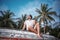 Stylish sexy young brunette man with a beard sits on an old wooden boat on a background of palm trees, vacation and travel concept